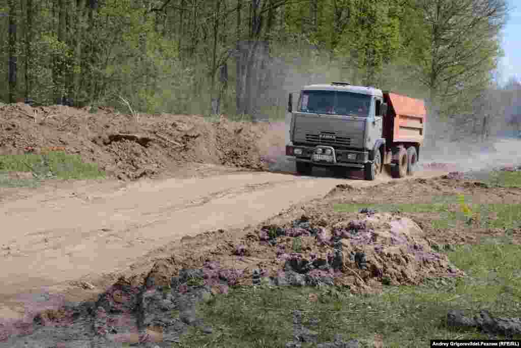 КАМАЗ свозит грунт, снятый с дороги, на лужайку. 