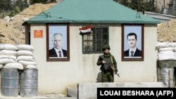 Військовий РФ між портретами президента Сирії Башара аль-Асада (праворуч) і очільника Росії Володимира Путіна на контрольно-пропускному пункті на околиці Дамаска, 1 березня 2018 року