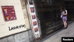 Par gleda izlog zatvorene trgovine pored zida sa kursnom listom i grafiom 'lopovi', Madrid, juni 2012.